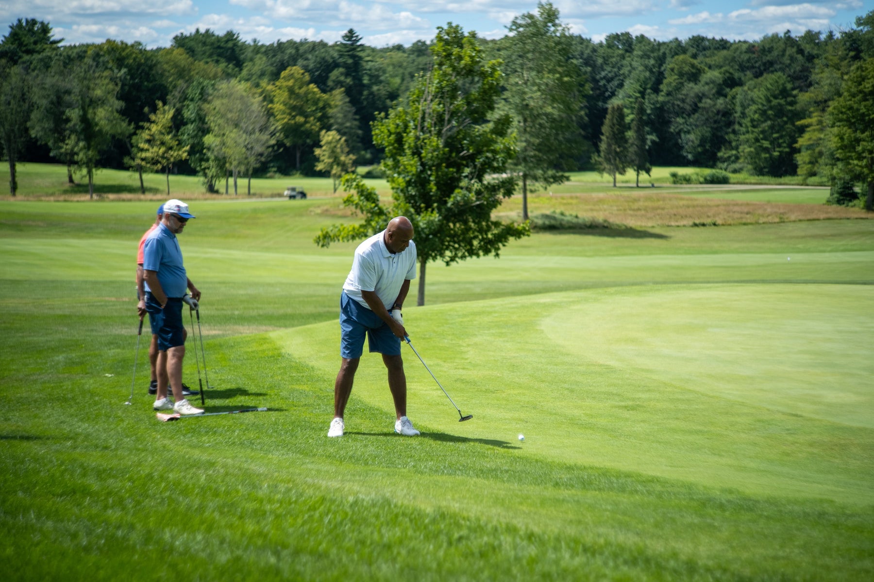 A golfer lines up his shot on the fairway while teammates look on